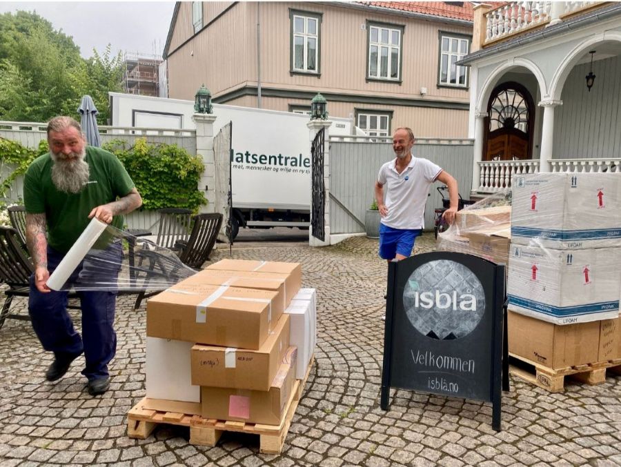 To menn ved siden av esker merket “Omega-3 kapsler” utenfor inngangen til isblå.no, klare for levering til Matsentralen.